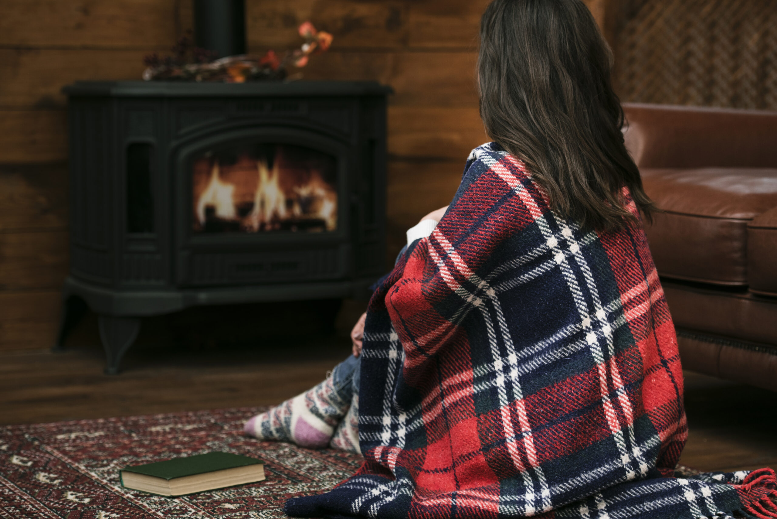 Cozy woman wrapped in blanket relaxing near fireplace