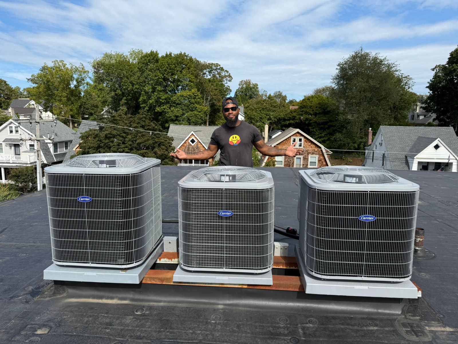 Man standing on a rooftop behind three outdoor air conditioning units.
